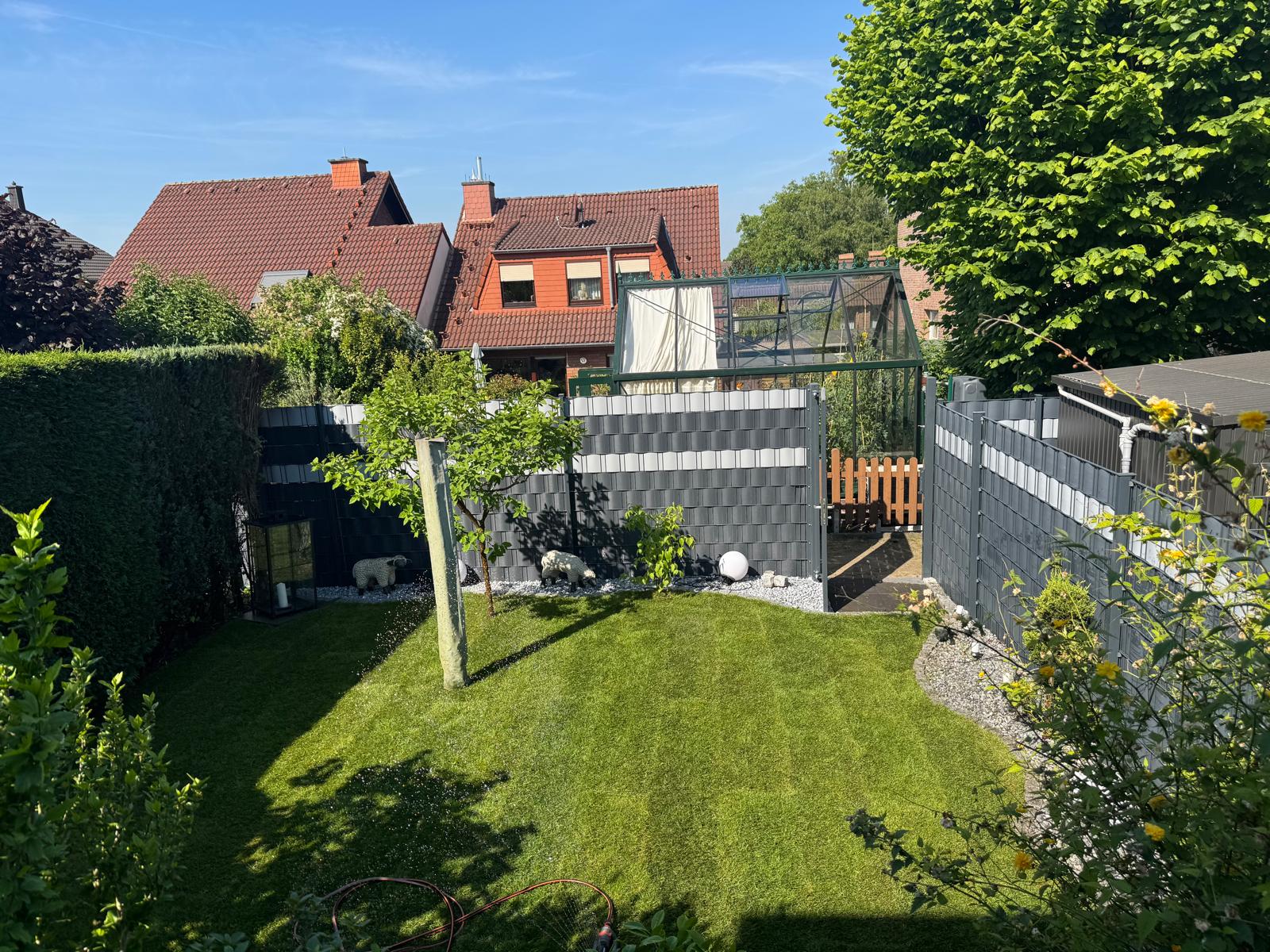 Ein gepflegter grüner Garten mit Rasen, Bäumen, grauem Zaun und zwei weißen Katzen