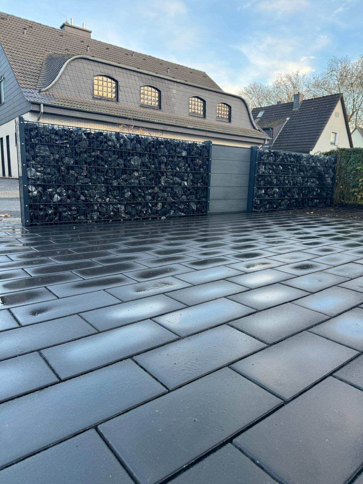 Eine modern gepflasterte, nasse Einfahrt vor einem Haus mit anthrazitfarbenen Steinen