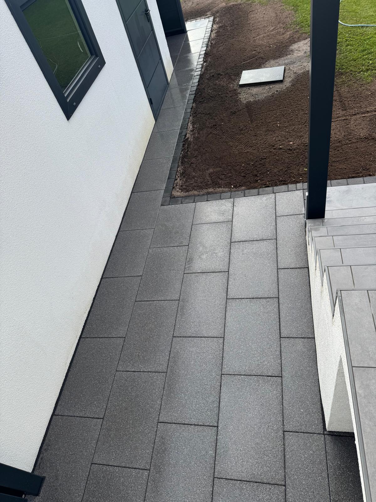 Graue Terrassenplatten neben weißer Hauswand und frischem Erdboden im Außenbereich